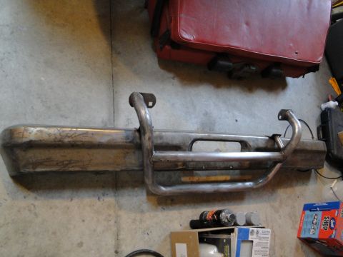1978 Ford Bronco - A metal front bumper with an integrated brush guard is shown, resting on a concrete floor.