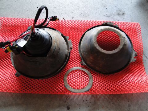 1978 Ford Bronco - Two headlight assemblies and a retaining ring are laid out on a red mat.