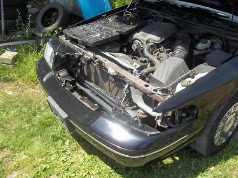 2004 Ford Crown Victoria - The front end of a black 2004 Ford Crown Victoria is visible, with the hood open to reveal the engine and damaged components.