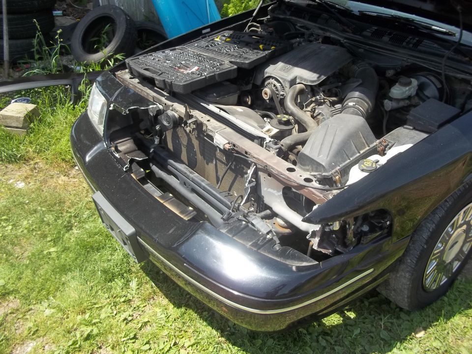 Black 2004 Ford Crown Victoria front end with hood open, showing engine and damaged radiator support