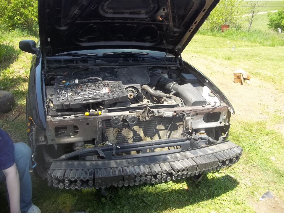 car with hood open showing engine, tools on top, front bumper removed