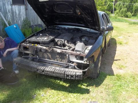 2004 Ford Crown Victoria - A black 2004 Ford Crown Victoria sits with its hood open, revealing the engine, as its front bumper is missing.