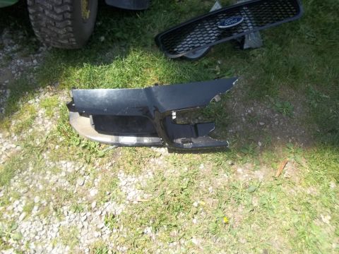 2004 Ford Crown Victoria - Damaged Ford bumper and grille parts are visible on the grass, with a tire from another vehicle in the background.