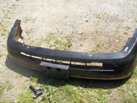 2004 Ford Crown Victoria - A detached front bumper assembly sits on the ground next to some grass and gravel.