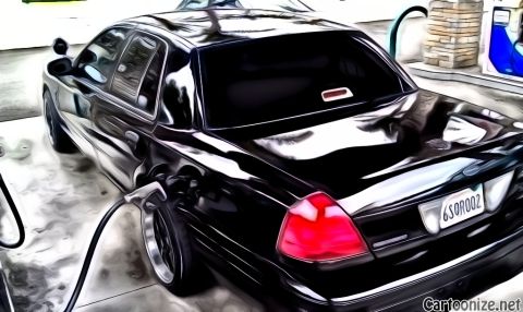 2003 Ford Crown Victoria - Black Panther sedan fueling at a station, fuel nozzle in filler; rear plate reads 6SOROOZ, dark wheels.