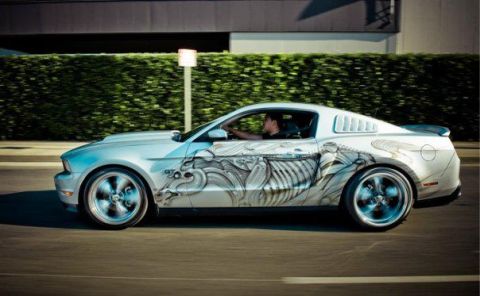 2007 Ford Mustang - A customized silver Ford Mustang with a skeleton graphic drives down the road, showing off its GT badge.