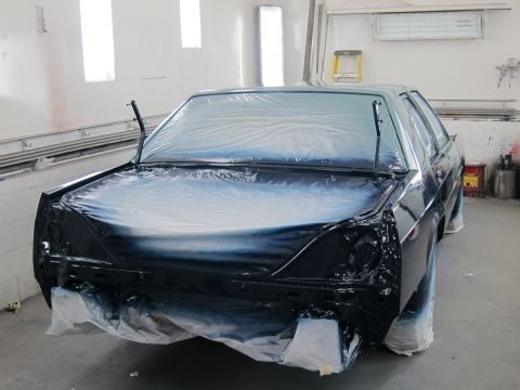 1991 Ford LTD Crown Victoria - A car is being prepped for painting inside a booth, with plastic covering most of its body.