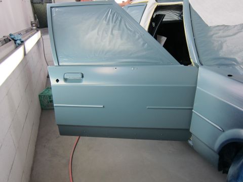 1991 Ford LTD Crown Victoria - A car door and fender are seen in a paint booth, with the door ajar and protective plastic covering parts of the vehicle.
