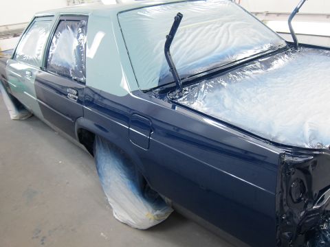1991 Ford LTD Crown Victoria - A dark blue sedan is seen from the side, with its windows covered in plastic as it is being painted.