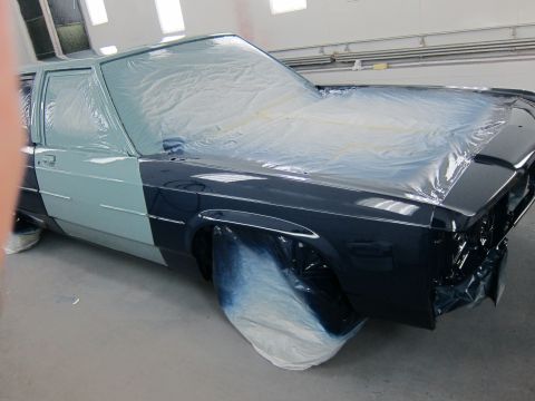 1991 Ford LTD Crown Victoria - A car is being prepped for painting in a booth, with plastic sheeting covering parts of the body.