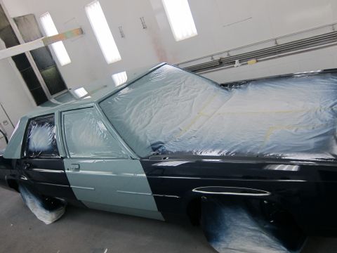 1991 Ford LTD Crown Victoria - A car is being prepped for painting in a booth, with plastic sheeting covering most of its body.