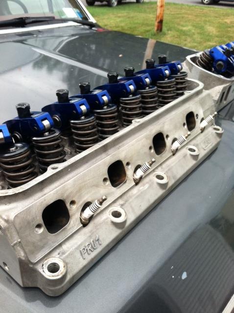 1991 Ford F-250 - Engine cylinder head with blue roller rockers and valve springs, resting on a vehicle's hood.