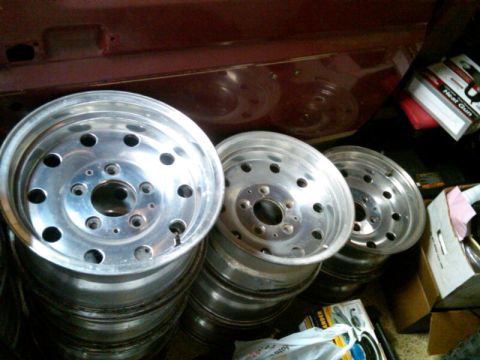 1986 Ford Bronco - A collection of aluminum wheels are piled up, with the interior of a vehicle visible above.
