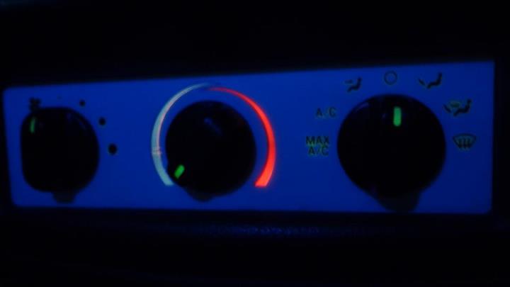 Climate control panel with three black knobs on a blue background. The middle knob has a red and white temperature indicator