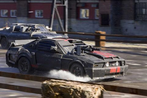 2007 Ford Mustang - Two heavily modified vehicles, one a muscle car with mounted guns, drive through a dusty area.