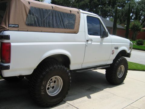 1992 Ford Bronco - A white 1992 Ford Bronco is shown with a tan soft top and lifted suspension.