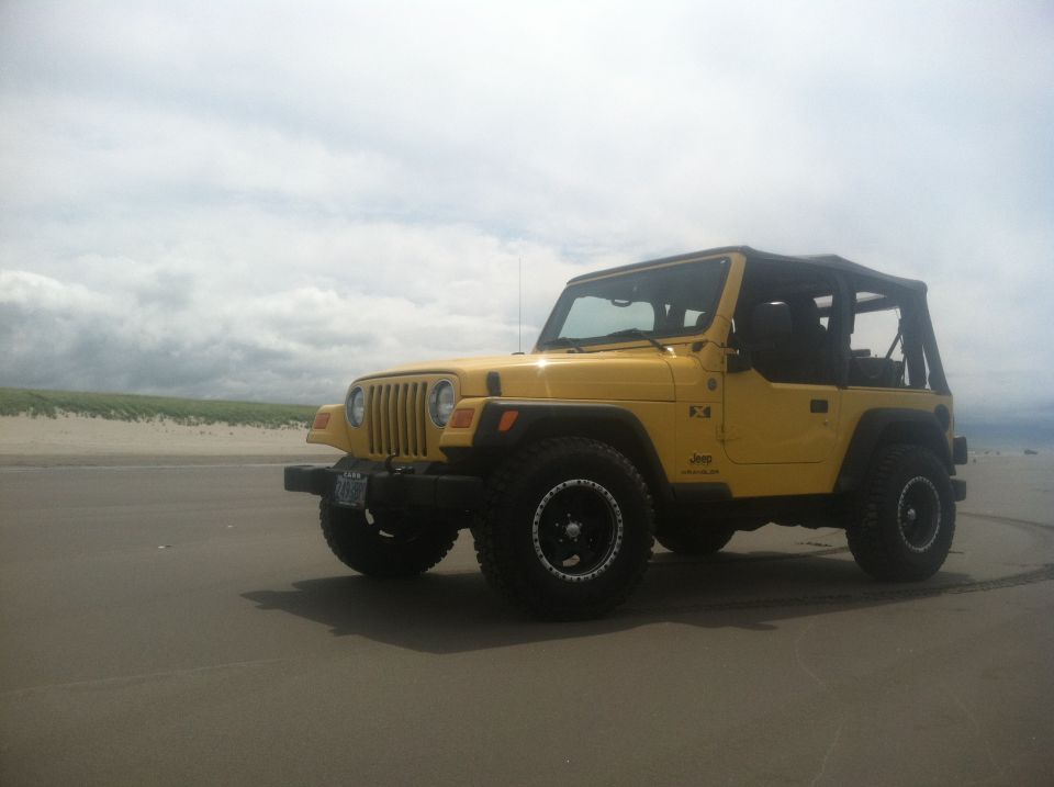 Yellow 2004 Jeep TJ on a beach with cloudy sky