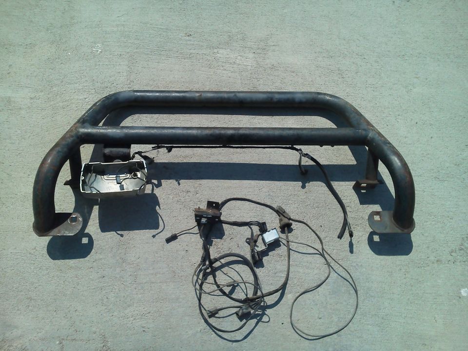Black metal pushbar with attached wiring harness and light housing, lying on concrete
