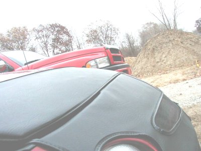 1997 Ford Taurus - A red pickup truck is partially visible behind a black convertible top, with a pile of dirt in the background.