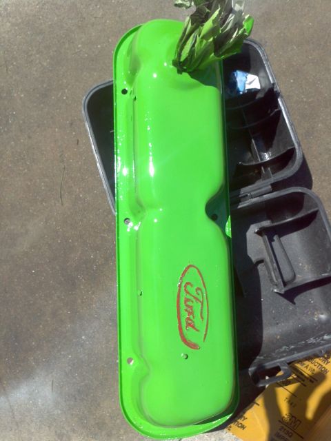 1987 Ford Bronco - A bright green Ford valve cover with a red Ford logo is shown next to a black plastic component.