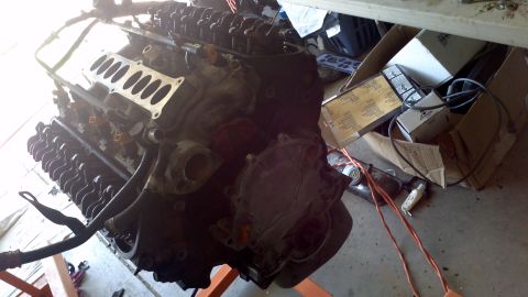 1987 Ford Bronco - A V8 engine is shown on an engine stand, with various boxes and electrical cords scattered around it.