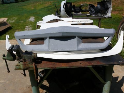 1976 Chevrolet Corvette - Various car body parts, including a front bumper, are laid out on a workbench for repair or modification.