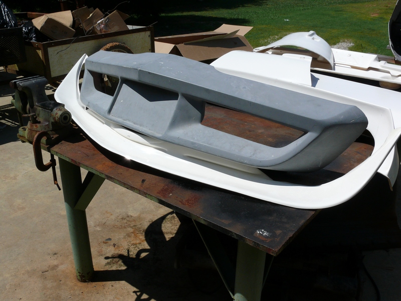 Gray car bumper part on a workbench with other white body kit pieces