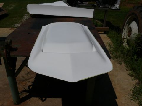 1976 Chevrolet Corvette - A white fiberglass hood scoop sits on a workbench, with a portion of a tractor wheel visible in the background.