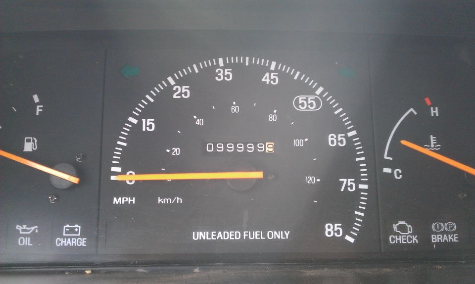 Car dashboard with speedometer, fuel gauge, temperature gauge, and warning lights. Odometer shows 0999999
