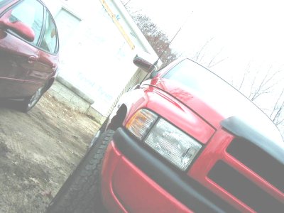 1997 Ford Taurus - Two vehicles, a red pickup and a red sedan, are parked outside on a dirt lot.