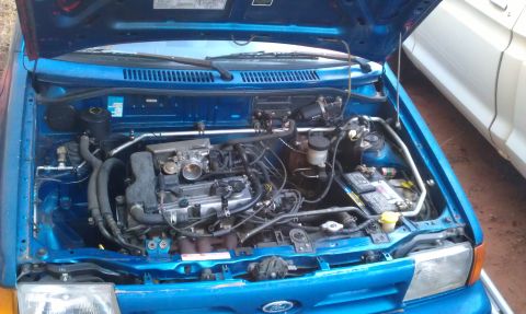 1991 Ford Festiva - The engine bay of a blue 1991 Ford Festiva is visible with the hood raised.
