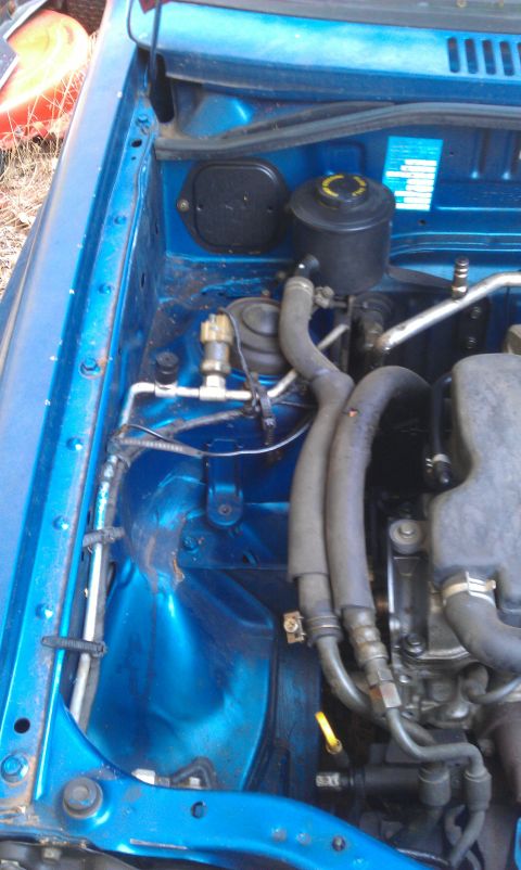1991 Ford Festiva - Close-up view of engine bay components, including hoses and a fluid reservoir.