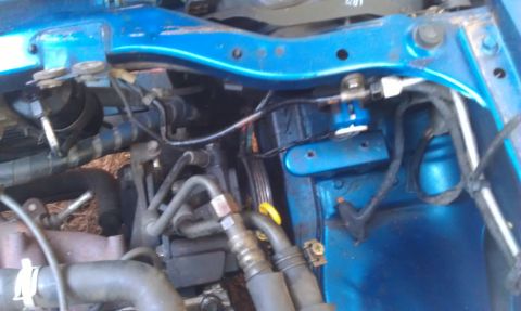 1991 Ford Festiva - Close-up view of various engine bay components, including hoses and wiring, under a blue painted panel.