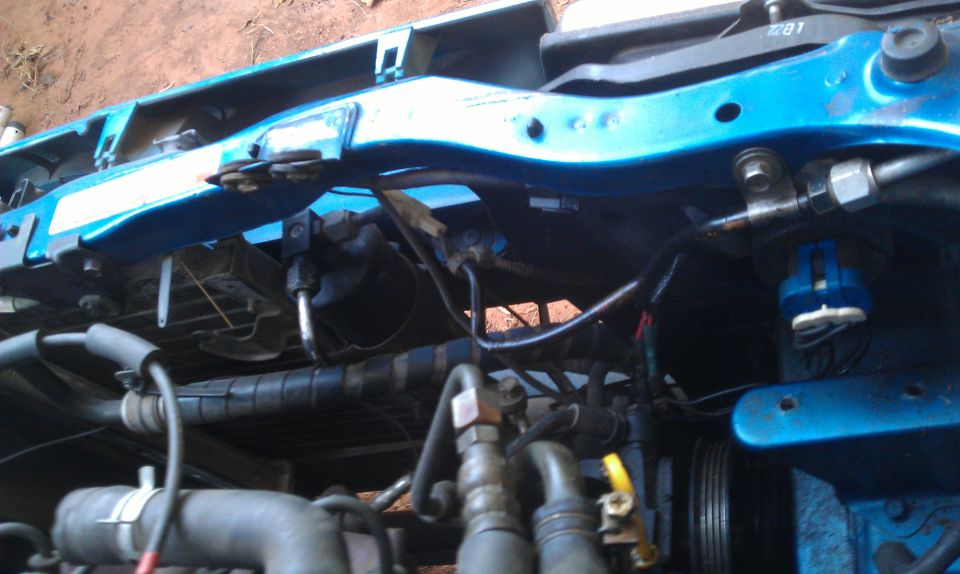 Close-up of engine bay hoses, metal lines, and blue painted frame components