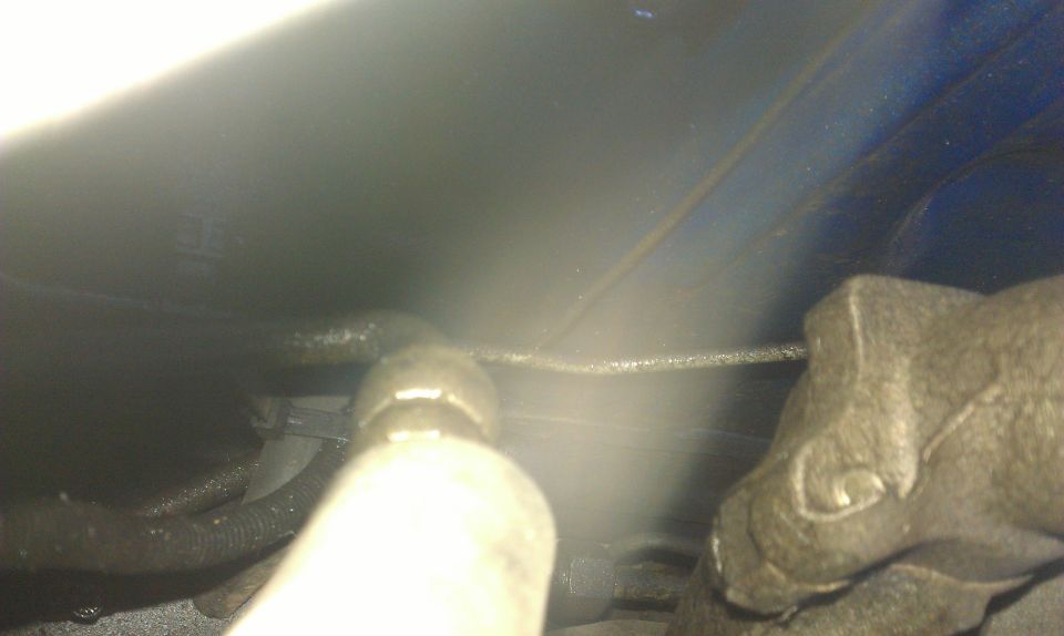 Close-up of a metal automotive part with hoses and a blue surface in the background