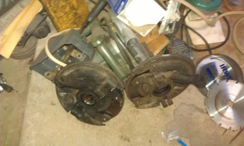 1991 Ford Festiva - Various car parts and tools are scattered on the floor, including two wheel hubs and a saw blade.