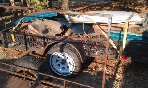 1991 Ford Festiva - A trailer carries disassembled car parts, including a blue fender and white roof panel, under a daytime sky.
