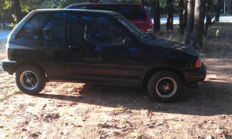 1991 Ford Festiva - Side view of a black hatchback with a red SUV visible in the background.