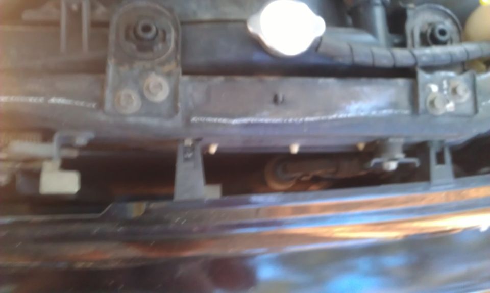Close-up of car radiator support with mounting hardware and a white cap
