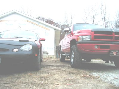 1997 Ford Taurus - Two vehicles, a red pickup truck and a dark car, are parked outside a garage.