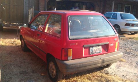 1991 Ford Festiva - Rear view of a red 1991 Ford Festiva, with a silver sedan visible in the background.