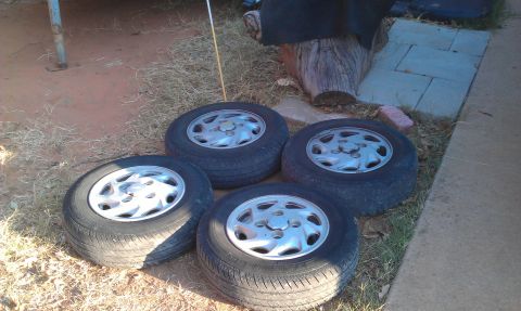 1991 Ford Festiva - Four tires and wheels are shown resting on the ground outdoors.