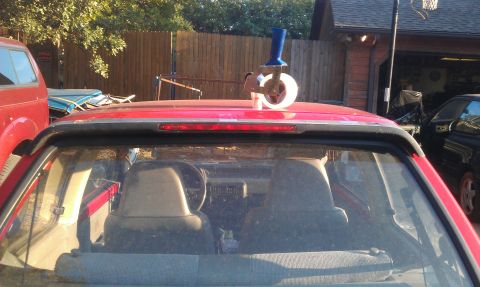 1991 Ford Festiva - A tape dispenser is attached to the roof of a red hatchback, seen from the rear.