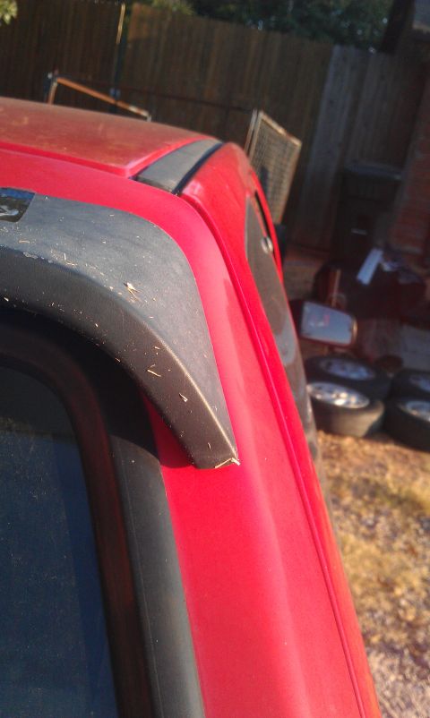 1991 Ford Festiva - Close-up of a red vehicle's roofline and trim, with a black plastic accent piece.
