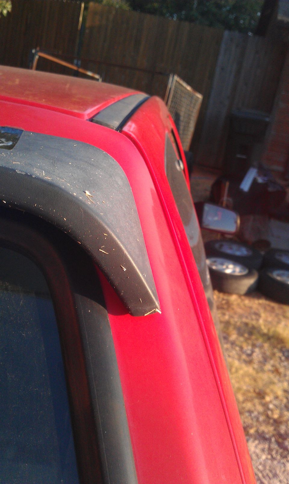 Red vehicle roof trim with black plastic accent. Some dirt visible
