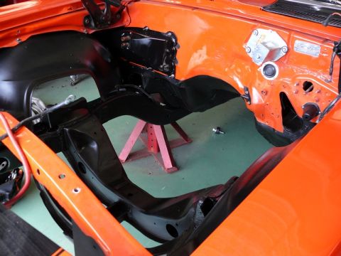 1968 Chevrolet Camaro - The engine bay of an orange car is shown during a restoration project, with the frame and inner fenders exposed.
