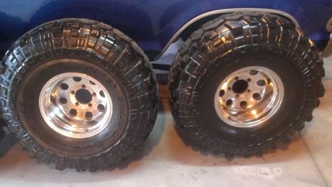 1978 Ford Bronco - Two off-road tires and rims are shown, with a portion of a blue vehicle visible behind them.