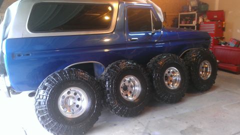 1978 Ford Bronco - A blue SUV is parked indoors with four oversized tires lined up beside it.
