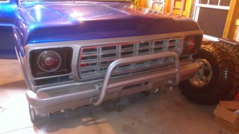 1978 Ford Bronco - Front view of a blue 1978 Ford Bronco with a chrome grille and brush guard, showing a large off-road tire.