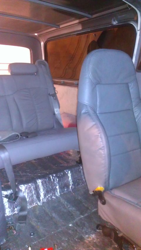 1978 Ford Bronco - The interior of a vehicle shows gray leather seats and the floor is covered with insulation material.
